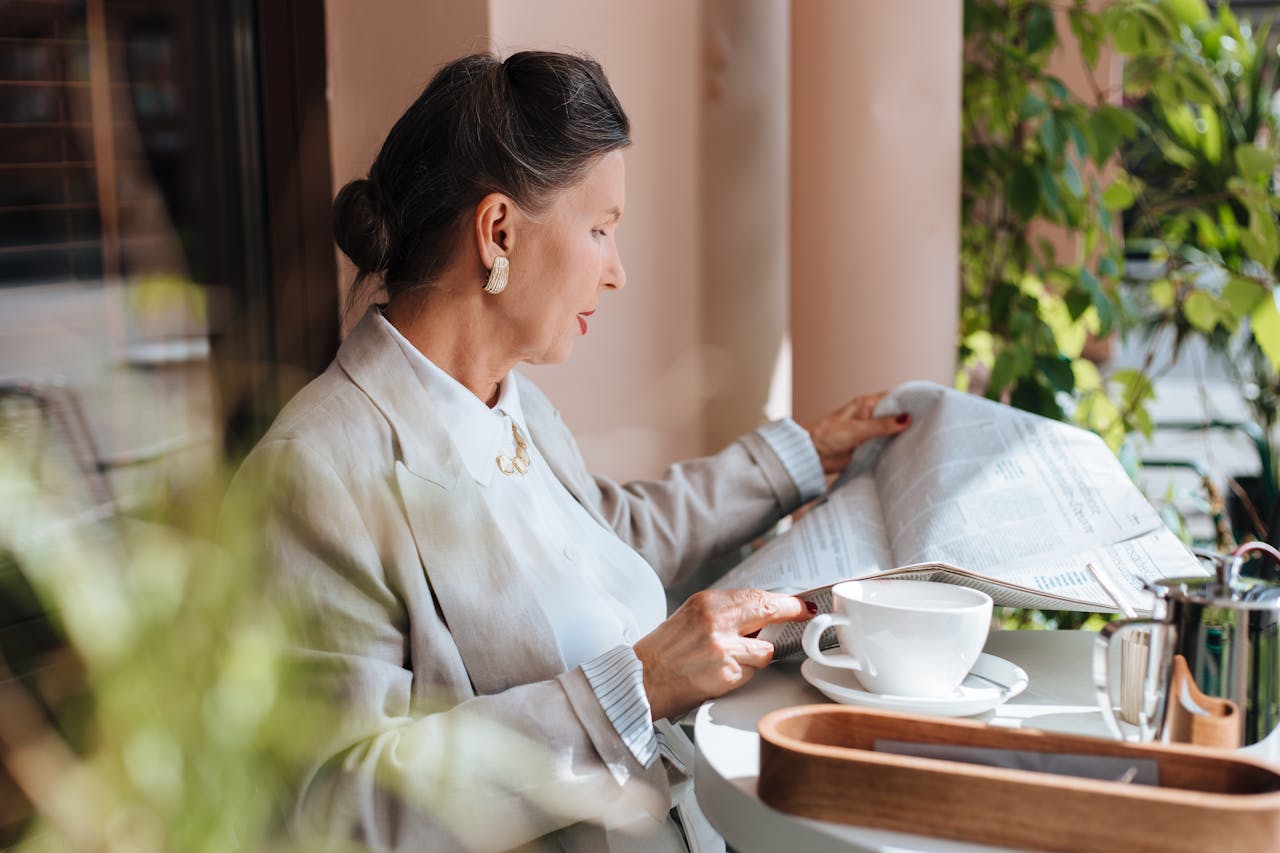 Sophisticated woman reading newspaper at a cafe table with coffee.