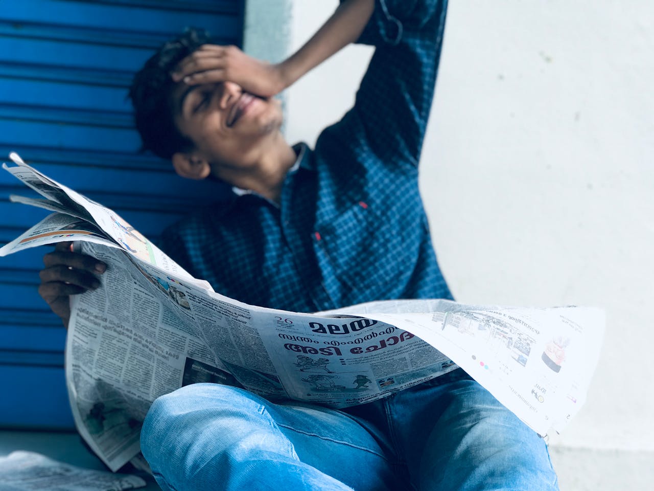 A young South Asian man casually reading a newspaper outdoors in Ernakulam, India.