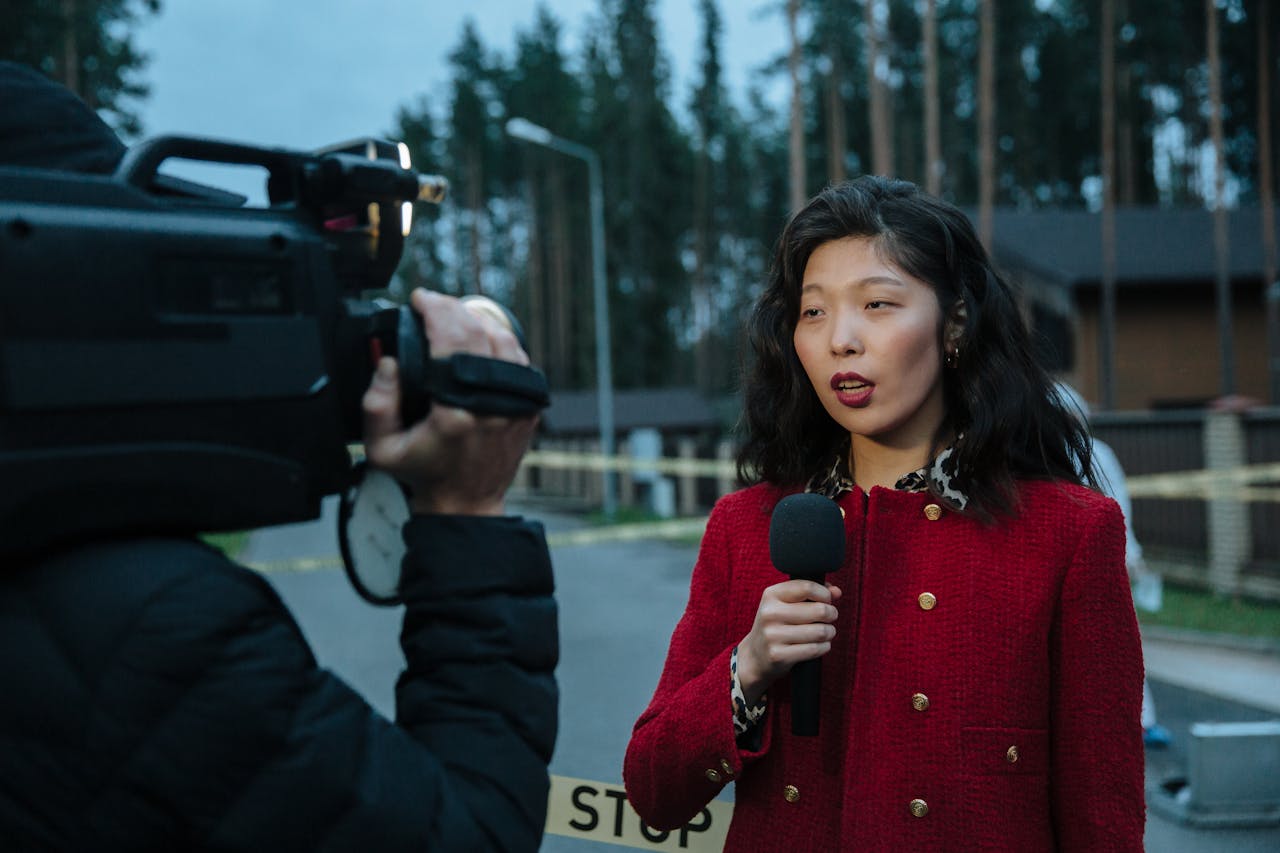 hero-img Asian female journalist reporting live from a suburban crime scene with camera and microphone.