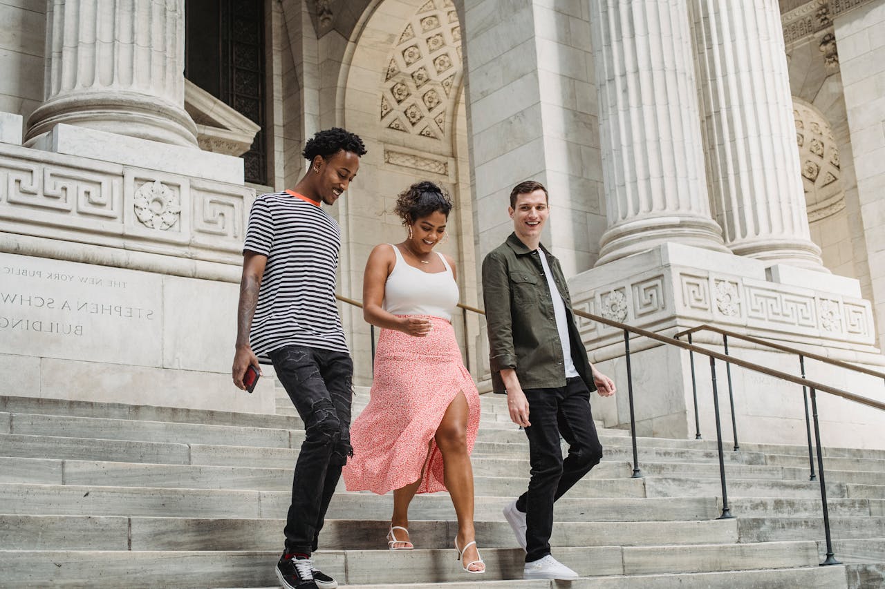 From below full body of content multiracial students walking downstairs of old university with massive columns on street in city