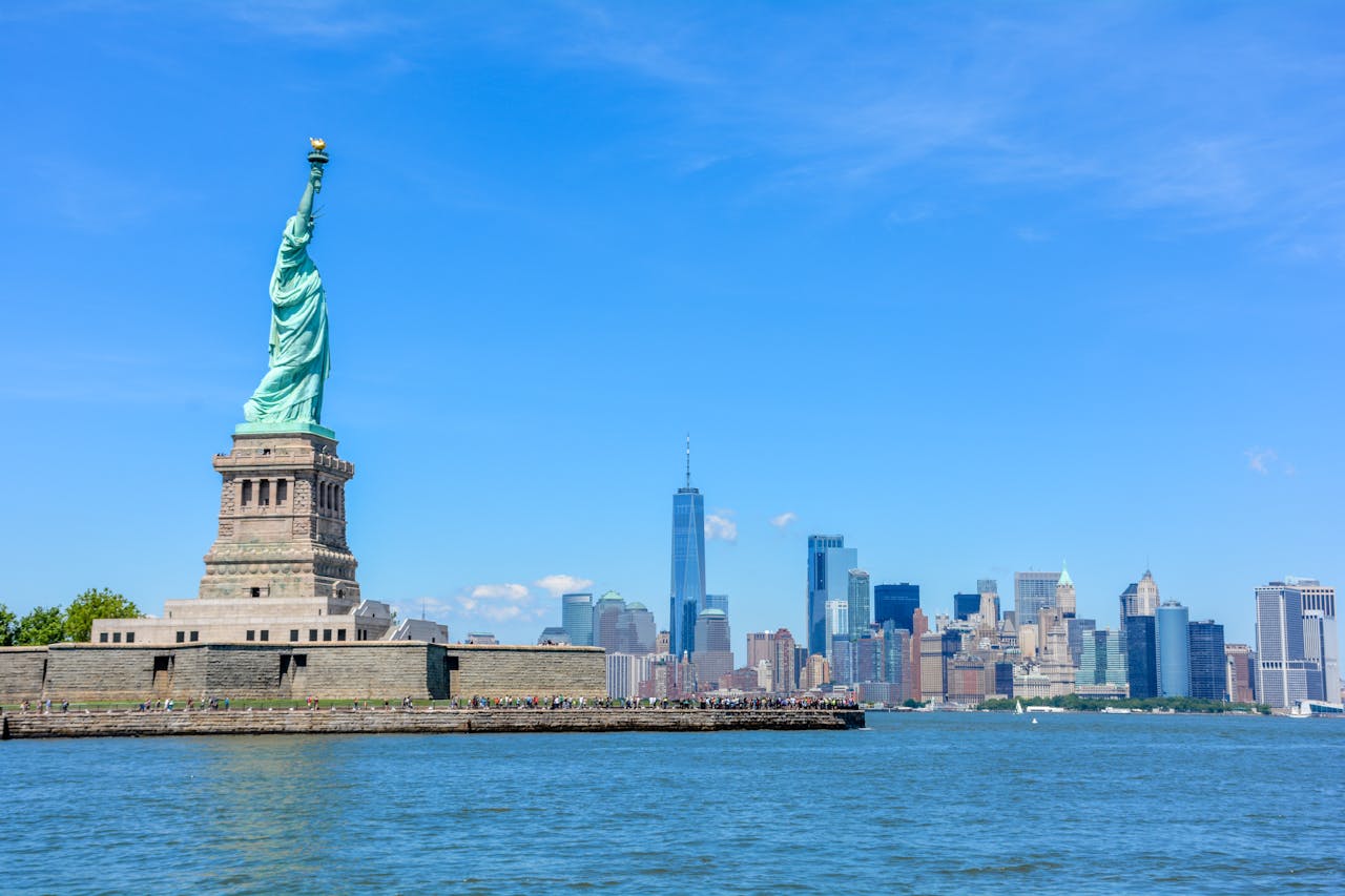 Home View of the Statue of Liberty against the New York City skyline and a clear blue sky.