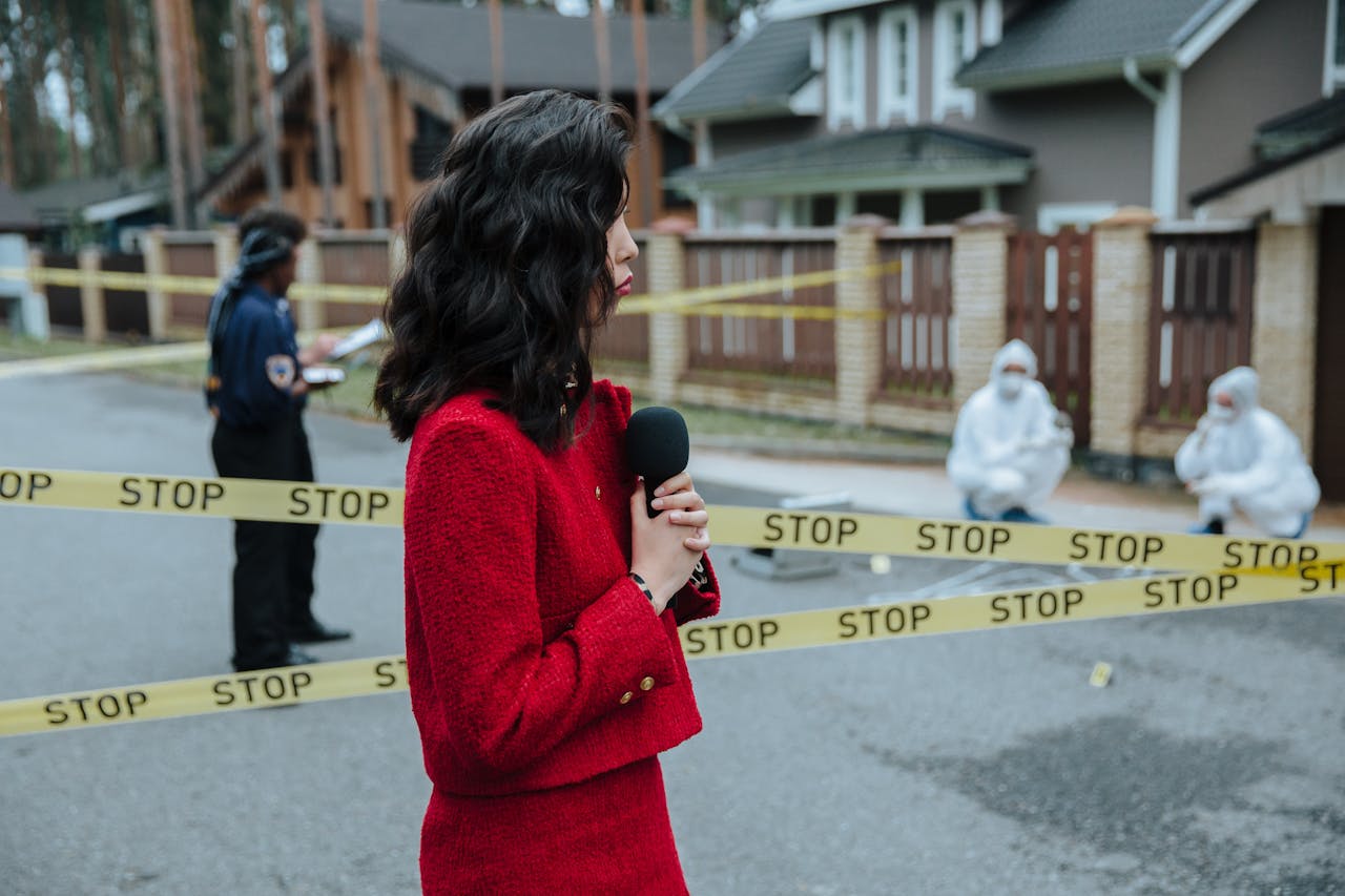 services-02 Female journalist reporting live on a crime scene investigation with police presence outdoors.