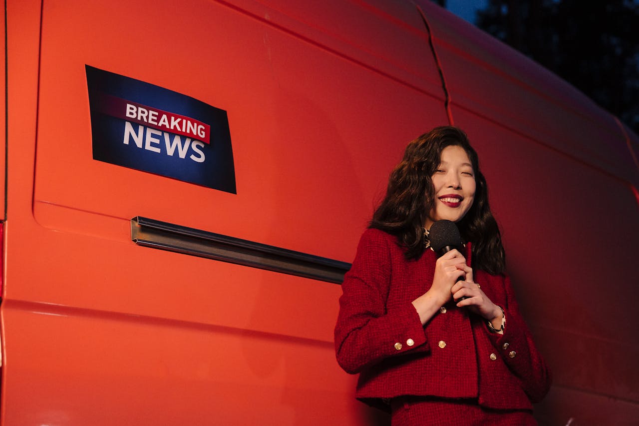 services-01 Asian female reporter smiling with microphone besides a news van at night.
