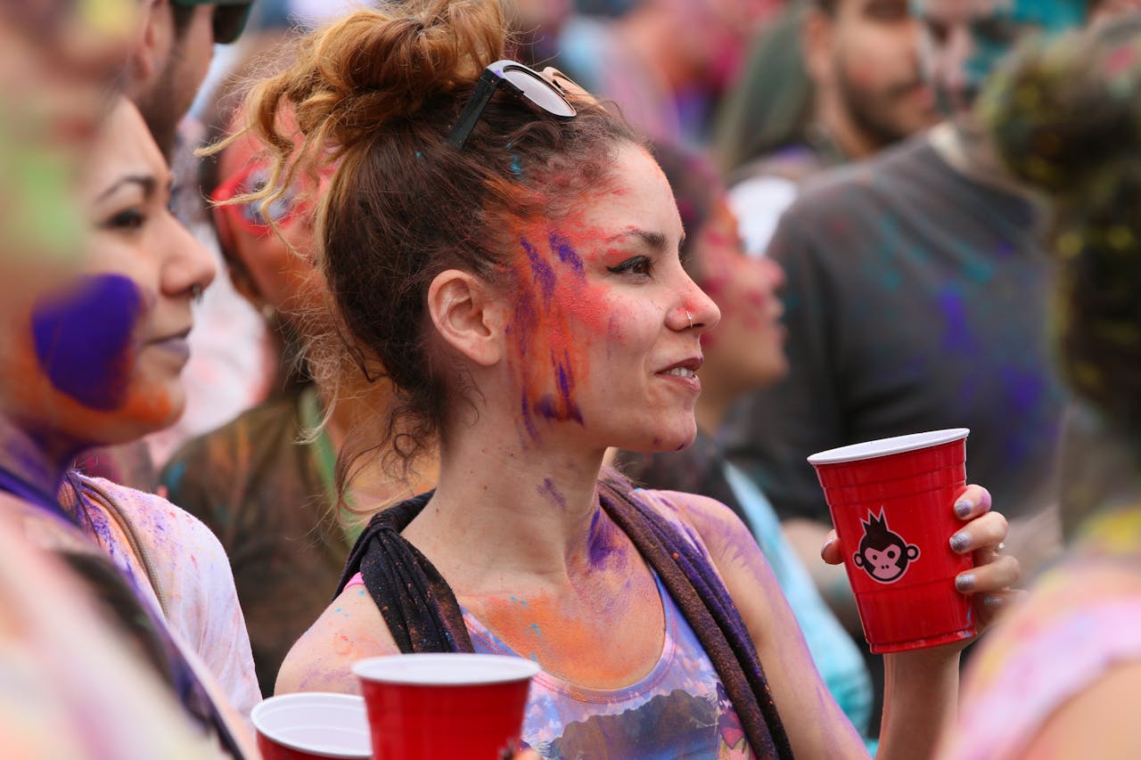 People enjoying a vibrant celebration with colorful face paints and drinks in New York.