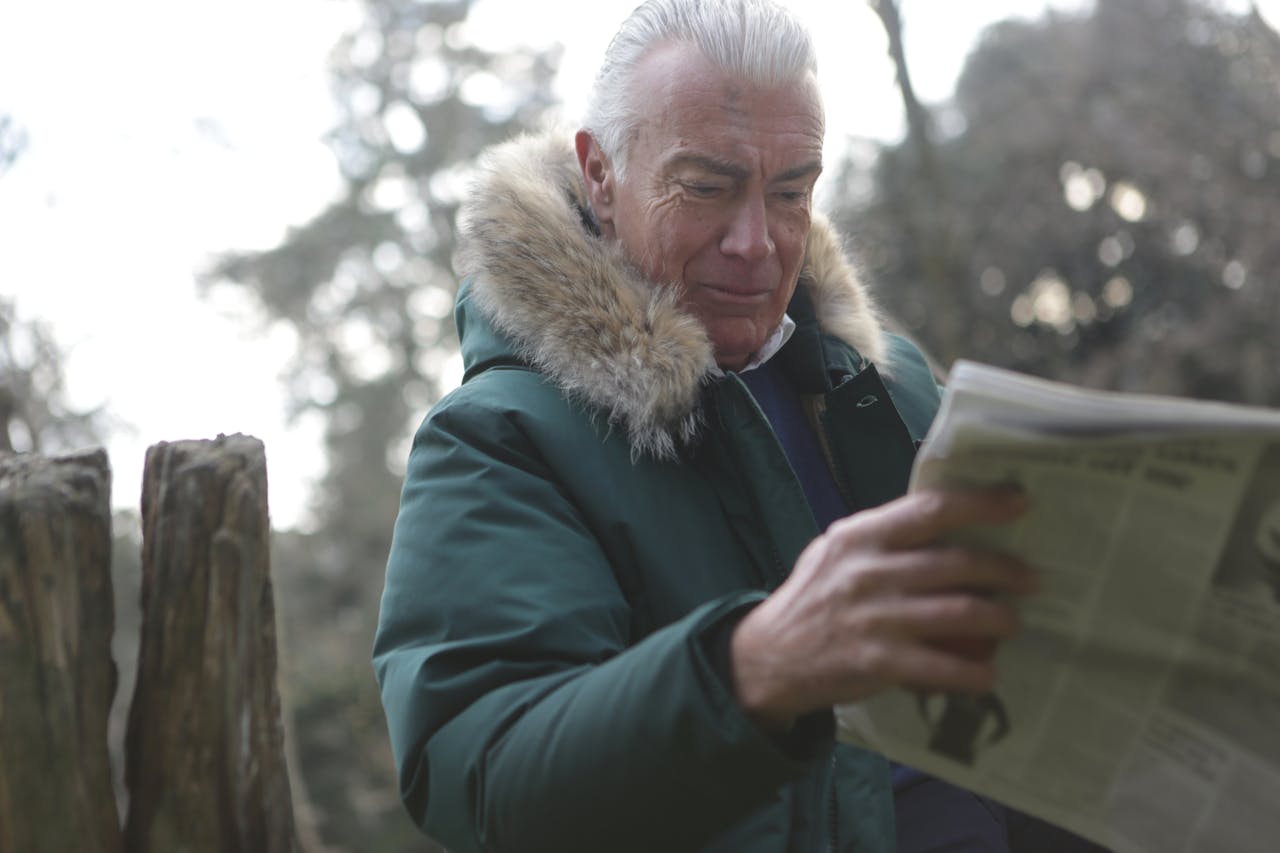 An elderly man in a winter coat reads a newspaper in a park, capturing a moment of relaxation.